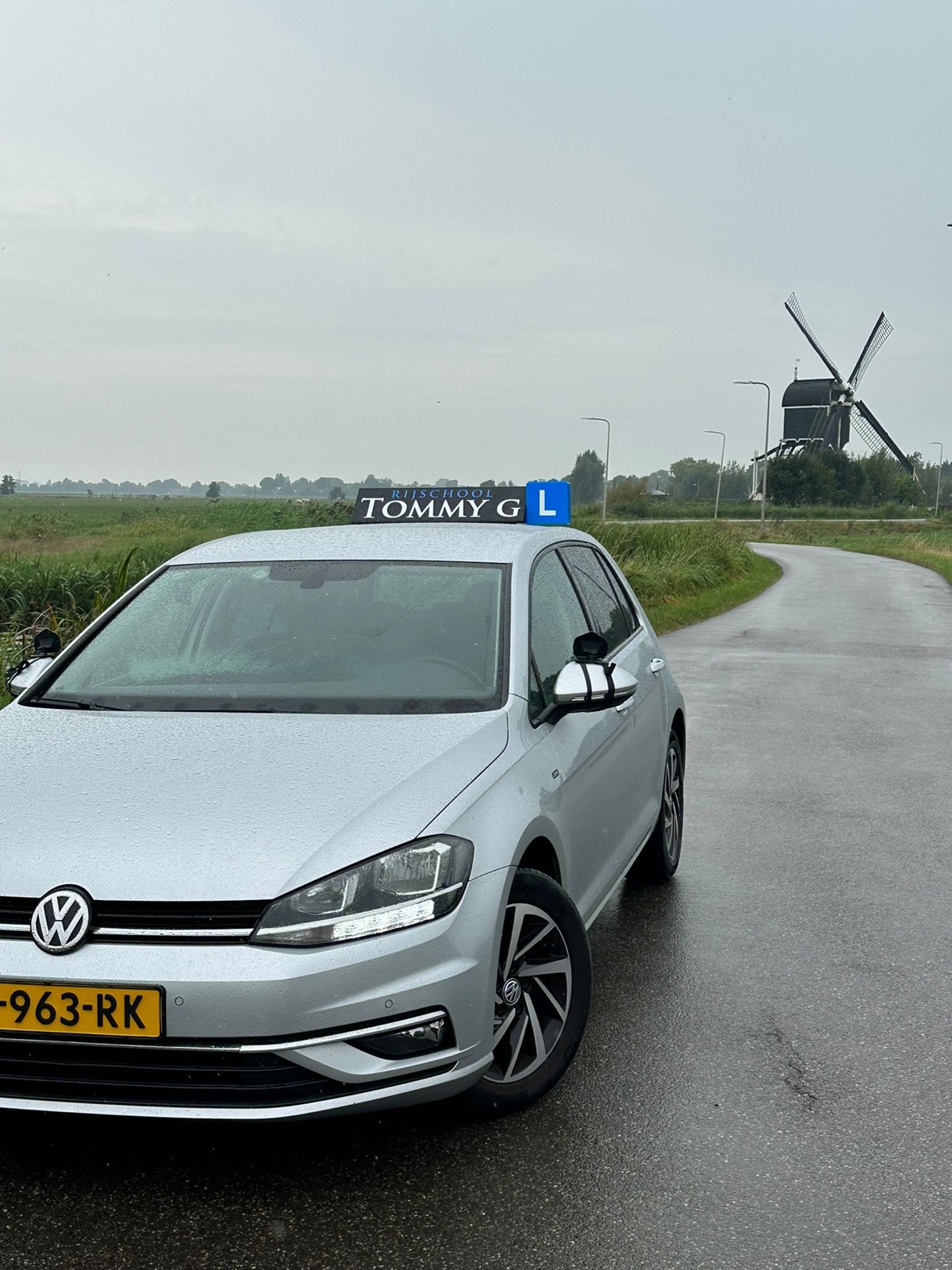 Lesauto op een polderweg met molen in de Krimpenerwaard